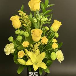 Tall yellow rose and lily arrangement in a black 'Best Dad Ever' mug on a wood slice base