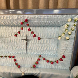 Red and white rosebud rosary draped inside a light blue open casket interior