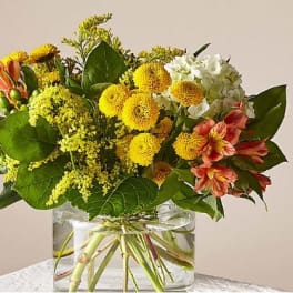 Low glass vase with yellow mums, white hydrangea, and orange alstroemeria in a compact bouquet.