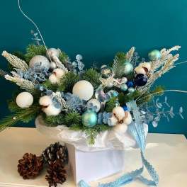 Holiday arrangement with pine, cotton bolls, and blue ornaments in a white box