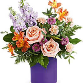 Mixed bouquet of roses, lilies, and purple flowers in a purple vase