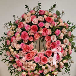 Large pink and peach rose wreath with satin bow displayed on a metal easel