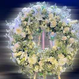 Large white floral wreath with roses and lilies displayed on a wooden easel