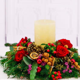 Red roses and holiday greenery arranged around a large pillar candle