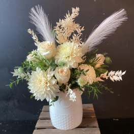White floral arrangement in a textured white vase with feathery accents