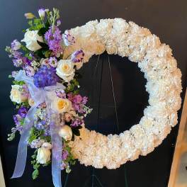 Large floral wreath on an easel with white and purple flowers and a lavender ribbon
