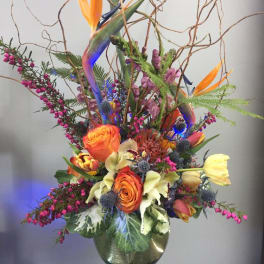 Tall mixed flower arrangement in a glass vase with orange and yellow blooms