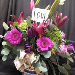 Pink and purple bouquet with lilies, gerbera daisies, and a LOVE sign in a decorative vase