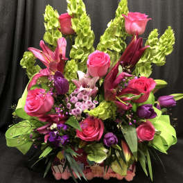 Bright pink roses and lilies arranged with green bells of Ireland in a gift box