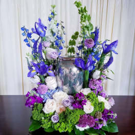 Tall floral arrangement with purple, blue, and white flowers around a silver vase