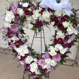 Heart-shaped floral wreath with white roses and purple flowers on a stand