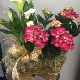 Pink hydrangeas and white calla lilies in a woven basket with a gold ribbon