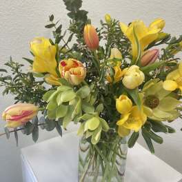 Yellow tulips and mixed blooms arranged in a clear glass cube vase