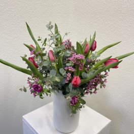Tall white vase with pink tulips and small purple flowers in a loose, airy arrangement