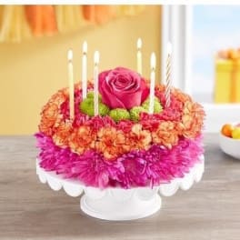 Round floral cake with a pink rose and candles on a white stand