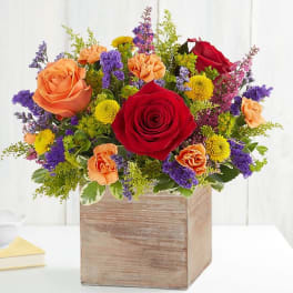 Mixed bouquet of red, peach, yellow, and purple flowers in a wooden box