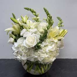 White roses, hydrangeas, and lilies in a clear glass bowl vase