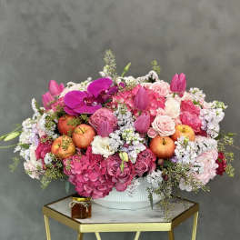 Pink floral arrangement with apples in a white bowl vase