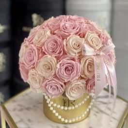Pink and cream roses arranged in a gold hatbox with pearl strands