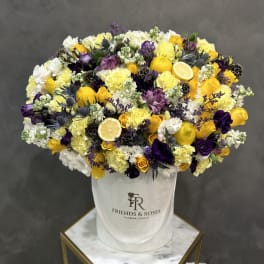 Large yellow, white, and purple flower arrangement in a white hatbox with lemon slices