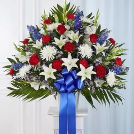 Standing floral spray with red and white flowers and a blue ribbon