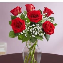 Red roses arranged in a clear glass vase with white filler flowers