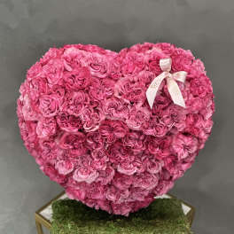 Heart-shaped arrangement of pink roses with a ribbon on a moss-covered base