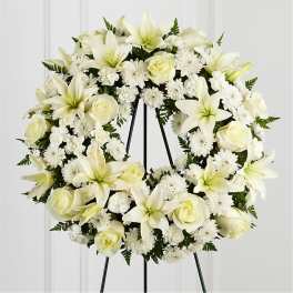 White floral wreath on a black stand with lilies, roses, and daisies