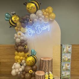 Bee-themed baby shower display with balloons, neon sign, and plush bees