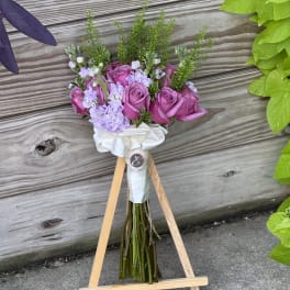 Pink rose bouquet with lavender flowers and white ribbon on a wooden stand