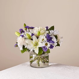 White lilies and daisies with purple filler in a clear glass vase