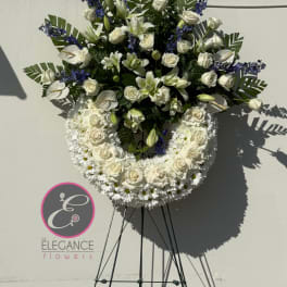 Standing white floral wreath with roses, lilies, and blue accents on an easel