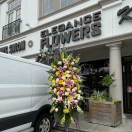 Tall standing floral spray with pink, yellow, and white flowers on a metal easel.
