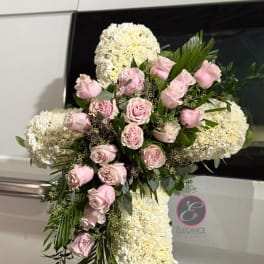 Pink roses and white floral spray arranged on a standing cross