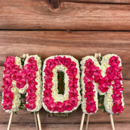 Floral standing tribute spelling MOM in pink and white flowers
