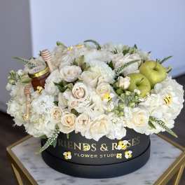 White roses and hydrangeas in a black hat box with green apples and honey jars
