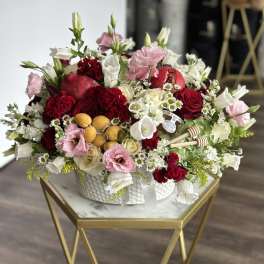 Mixed red, pink, and white floral arrangement in a white bowl with pomegranates and honey dippers