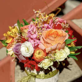 Colorful mixed bouquet with an orange rose and assorted blooms in a white pot with a ribbon bow