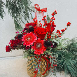 Red roses and gerbera daisies in a gold vase with berry stems