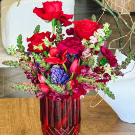 Red roses and mixed blooms arranged in a red glass vase