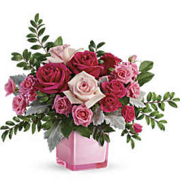 Pink and white roses arranged in a pink glass vase
