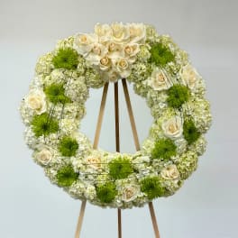 Circular floral wreath of white roses and green mums on a wooden easel