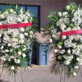 Two white funeral standing sprays with pink ribbons on easels
