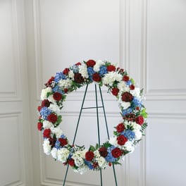 Circular floral wreath on a metal stand with red, white, and blue flowers