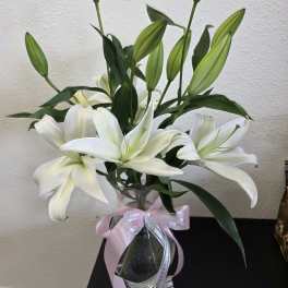 White lilies in a clear glass vase with a pink ribbon