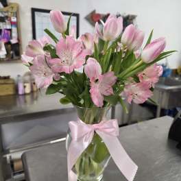 Pink tulips and alstroemeria in a glass vase with a pink ribbon