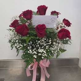 Red roses arranged in a glass vase with baby's breath and a pink ribbon
