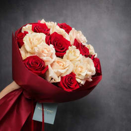 Hand-tied bouquet of red and cream roses wrapped in dark red paper.