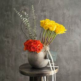 Yellow and orange roses in a gray vase with tall eucalyptus stems