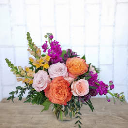 Bouquet of peach and blush roses with purple flowers in a glass vase